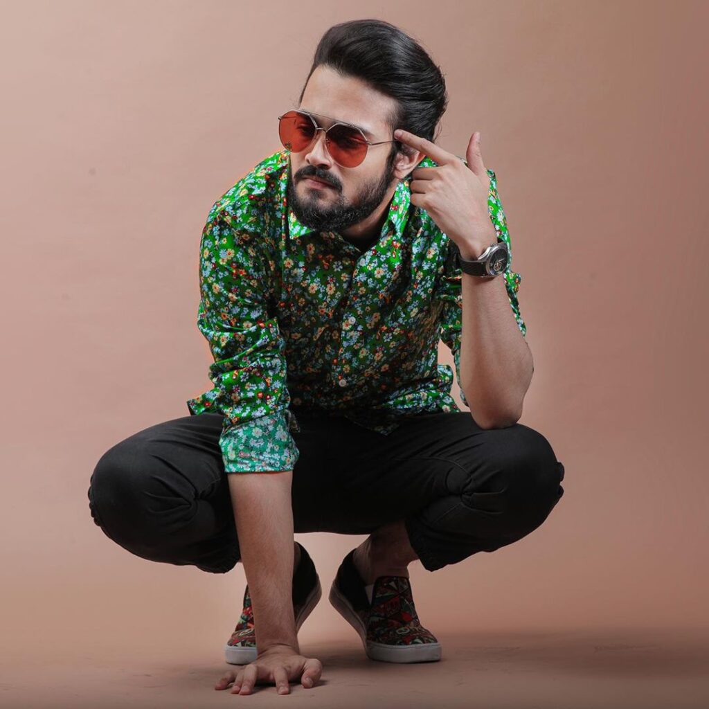 Bhuvan Bam  Hairstyle - posing in a green tshirt and wearing black trouser, brown shoes ..sitting like a duck..