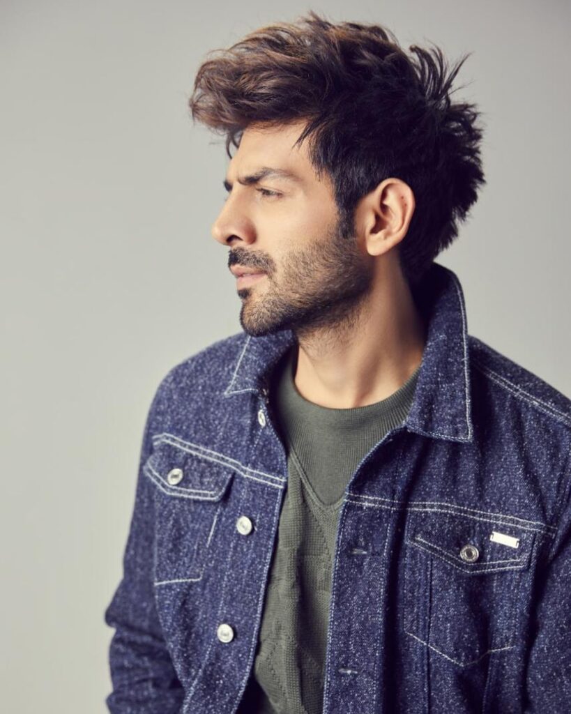 Kartik Aryan Hairstyle - posing for camera - facing other side of the camera, not facing. Wearing denim jacket, and tshirt.