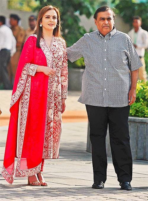 Mukesh Ambani Weds November Born Nita - Both are standing together in picture. Mukesh Ambani wears Black check shirt and trouser and Nita Ambani red suit