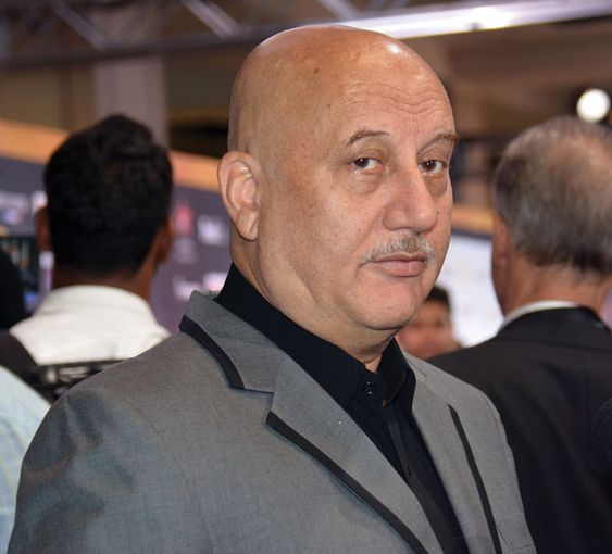 Anupam Kher wearing grey coat with black shirt in standing pose