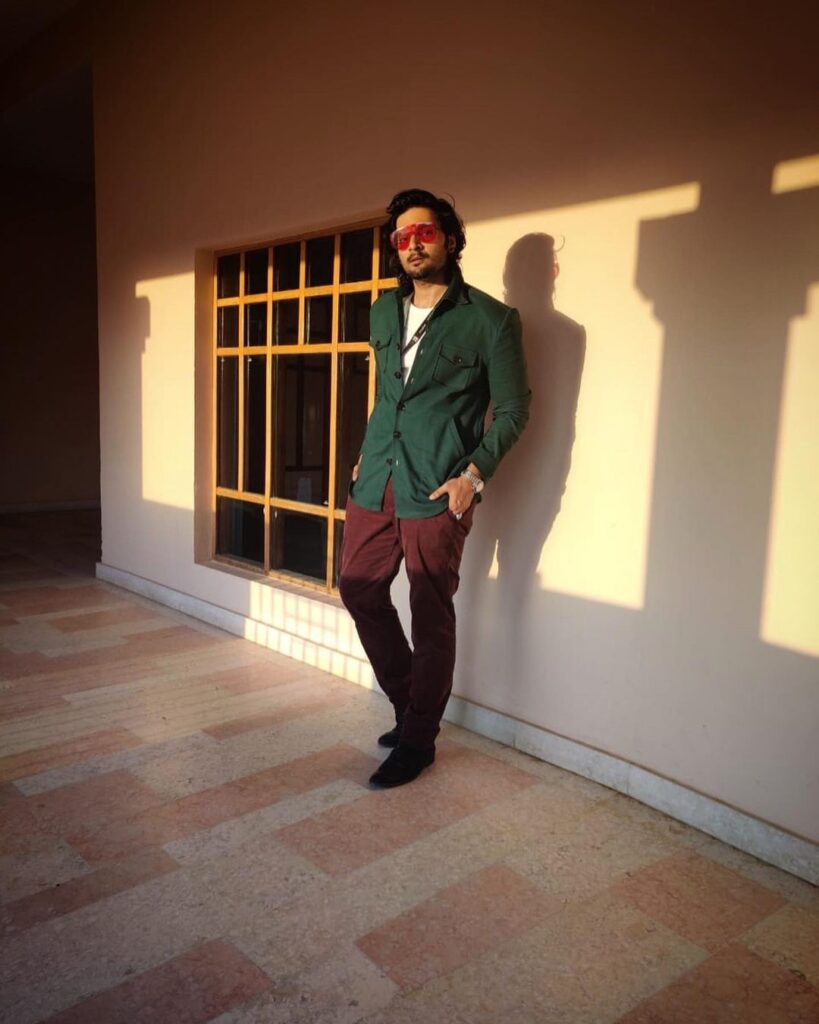 Ali Fazal pose with long classy hairstyle & standing in front of wall