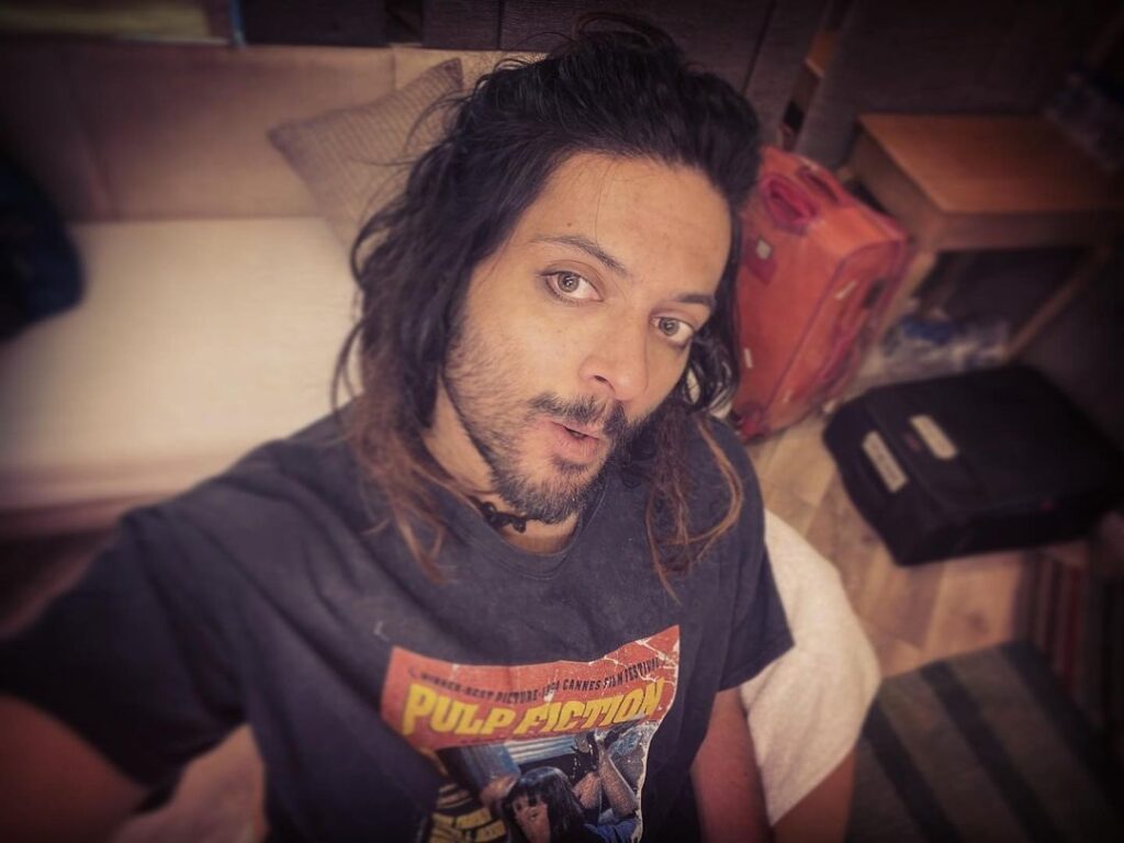 Ali Fazal pose with long hair with highlights hairstyle with black tshirt