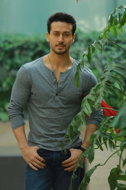 Tiger Shroff standing in garden and wearing grey tshirt & blue jeans