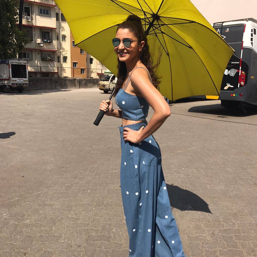 Smiling Anushka in blue and white trouser and crop top carrying a yellow umbrella -  Anushka Sharma Hairstyles