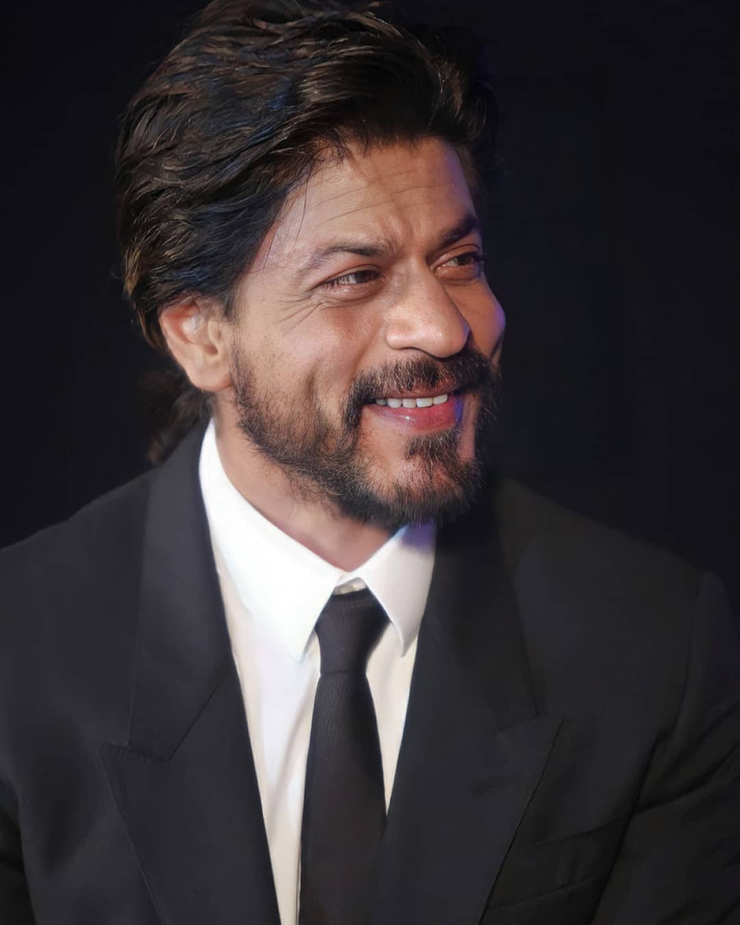 Smiling Shahrukh khan in black suit and white shirt showing his ponytail look - shahrukh khan best hairstyles