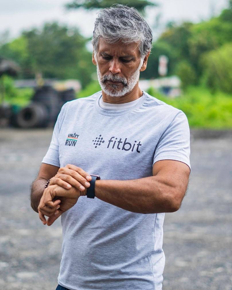 Milind Soman in sky-blue t-shirt looking at this watch - Milind Soman latest Hairstyle