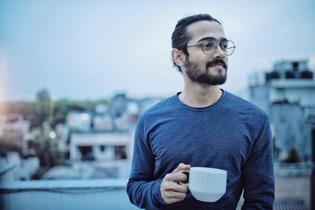 In Blue t-shirt Bhuvan Bam is holding a coffee mug and smiling - Bhuvan Bam hairstyle 2021