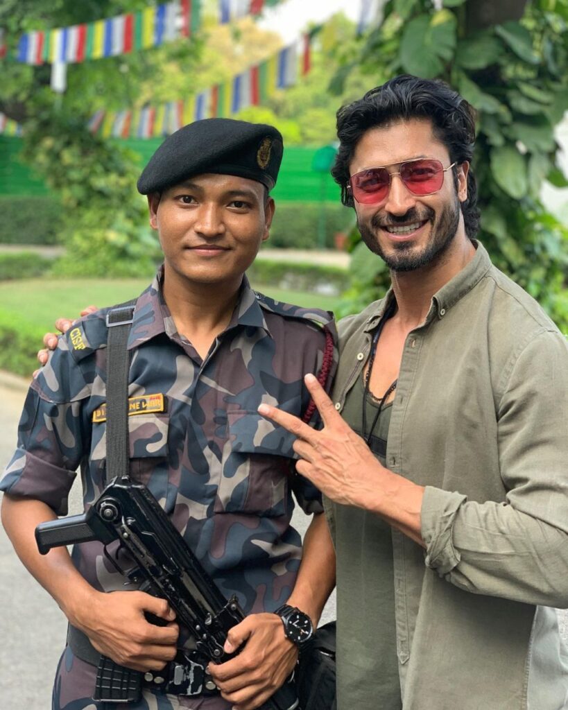 Smiling Vidyut Jammwal in goggles posing with an army man - Vidyut Jammwal curly hairstyle