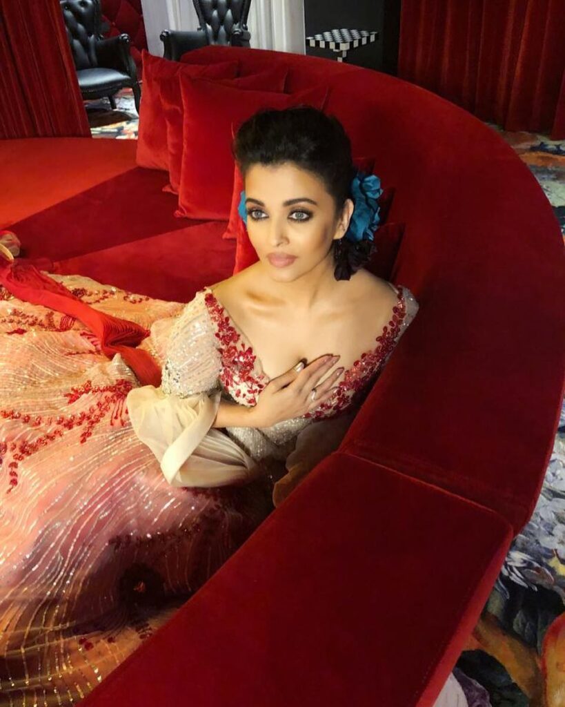 Aishwarya Rai in golden and red deep neck dress with Puff bun with accessories posing for camera - celebrity hairstylist