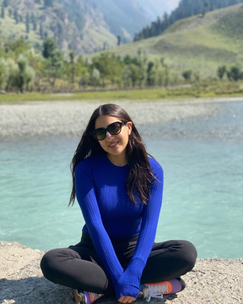 Sara Ali Khan in blue top and black bottom with goggles sitting at the bank of river - Sara Ali Khan Hairstyles
