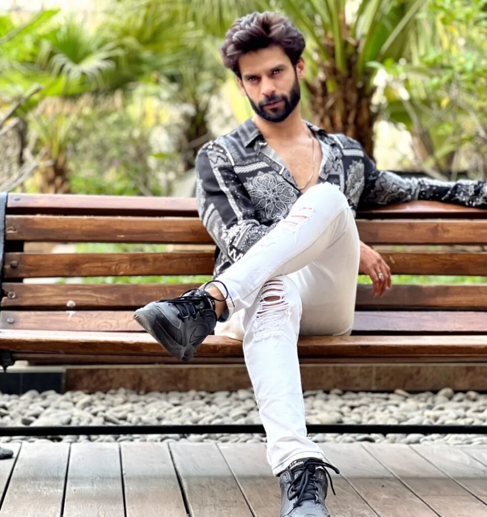 Gaurav Arora sitting on a bench in black and white printed shirt with white bottoms - models in India