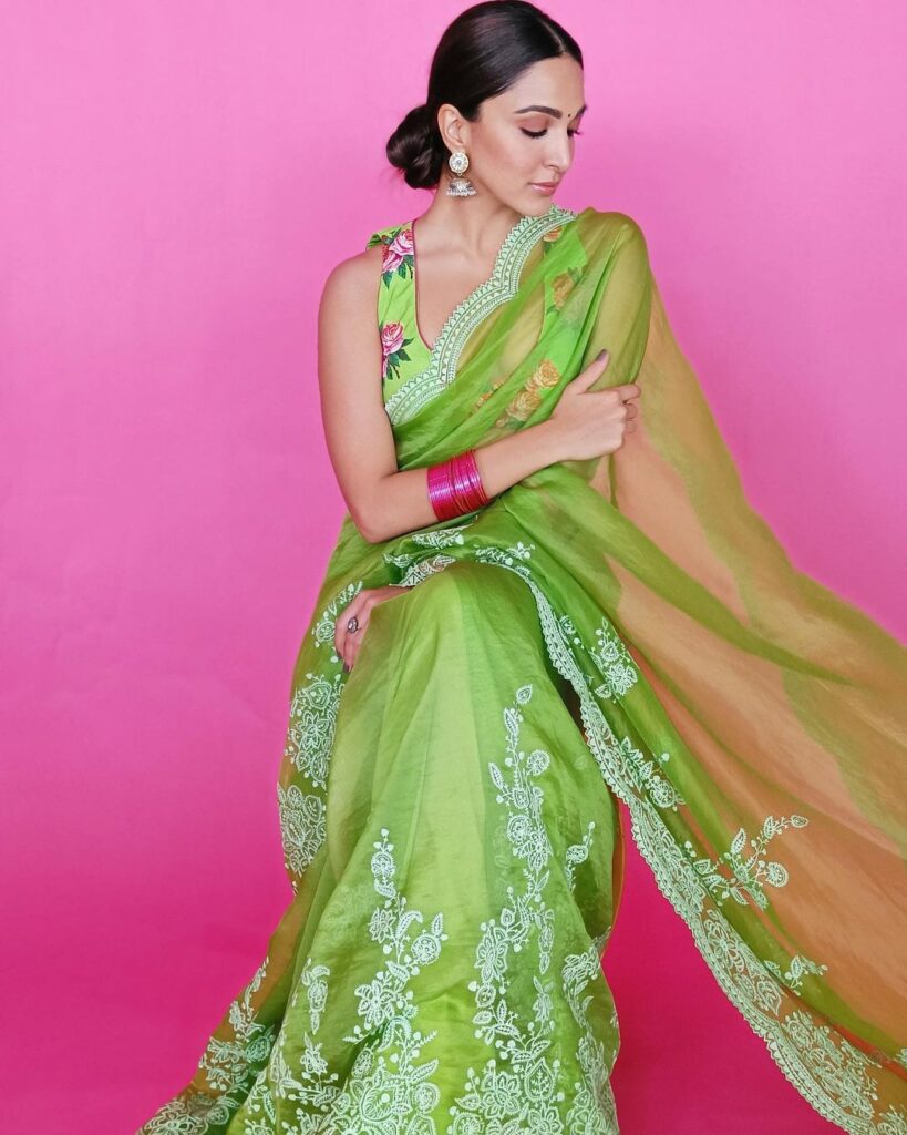 Kiara Advani in green saree and floral printed blouse posing for camera and showing her Middle parted low bun - hairstyles in saree