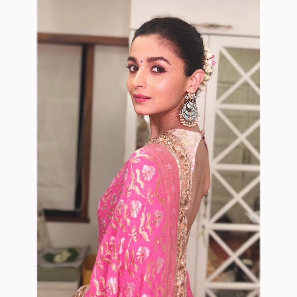 Alia Bhatt in pink and off white saree with danglers posing for camera and showing her Sleek and Tight Bun - alia bhatt face shape