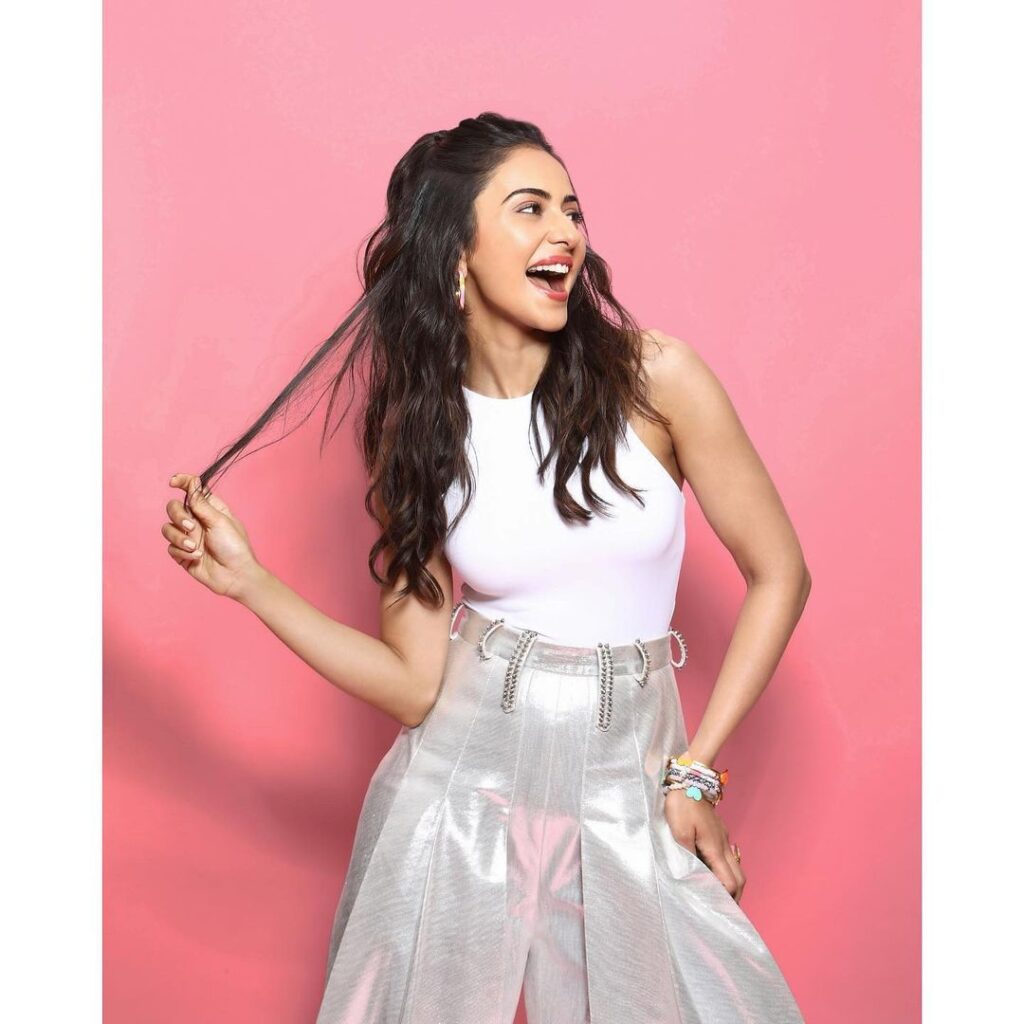 Smiling Rajul Preet Singh in white top and silver skirt posing for camera and showing her half tie hairstyle - Rakul Preet Singh hairstyles