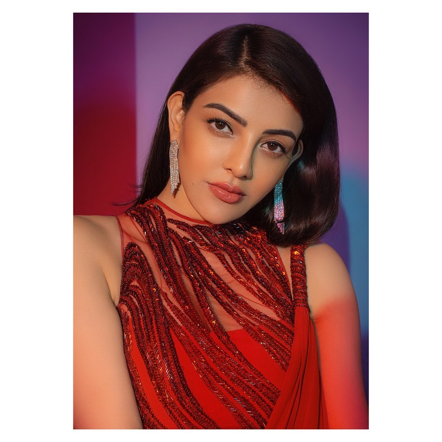 Kajal Aggarwal in red cut sleeves top with long earing posing for camera and showing her Side parted voluminous hair - Kajal Aggarwal Straight hair