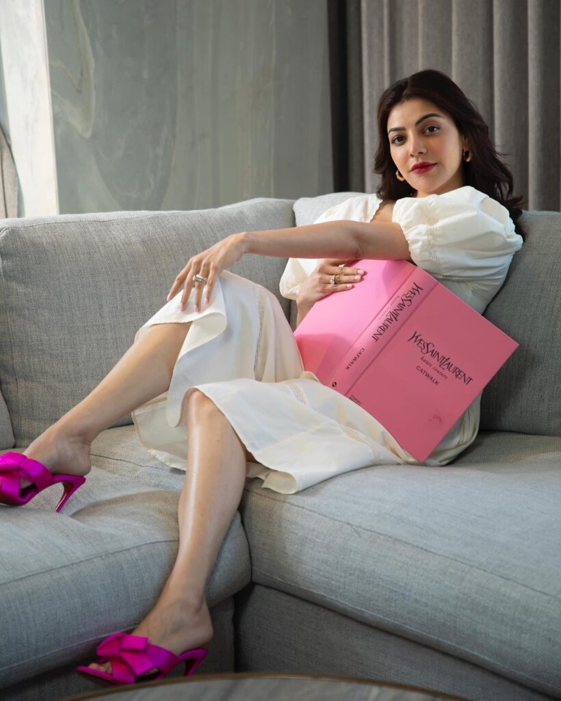Kajal Agarwal in white knee length dress with purple sandals sitting on a couch - kajal aggarwal trendy hairstyle