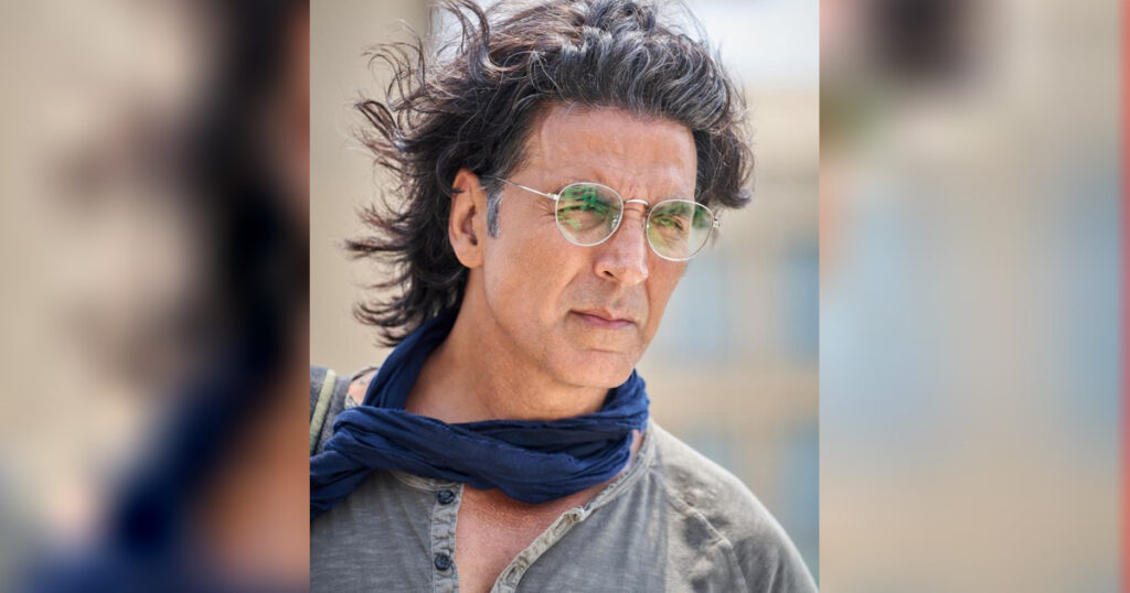 Akshay Kumar in grey shirt with blue scarf poisng for camera and showing his long hair - akshay kumar hairstyle name