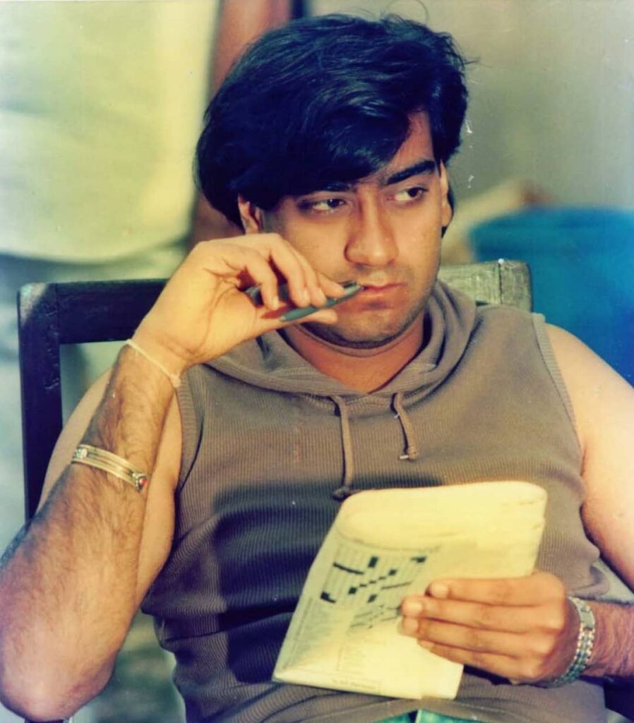 Ajay Ddevgan wearing a grey cut sleeves t-shirt and sitting on a chair, thinking about something - hairstyle ajay devgan