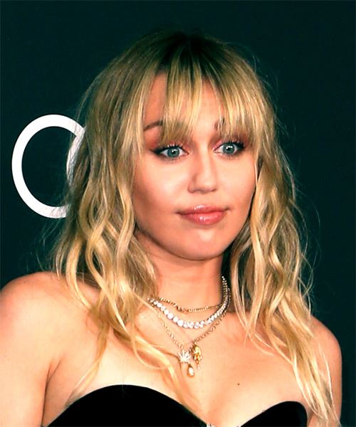Miley Cyrus in black off shoulder dress posing for camera and showing her curls with bangs - hollywood actress hairstyle