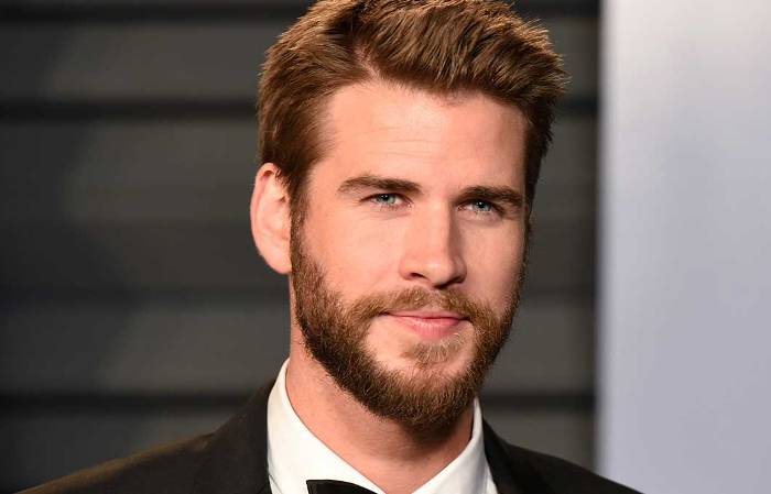 Smiling Liam Hemsworth in black coat with white shirt with black bow tie posing for camera and shoeing his side-parted Pompadour - hairstyles of Hollywood actors