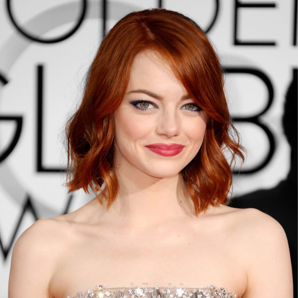 Emma Stone in off shoulder dress and lipstick posing for camera and showing her brunette hair with bangs - hollywood actress hairstyles