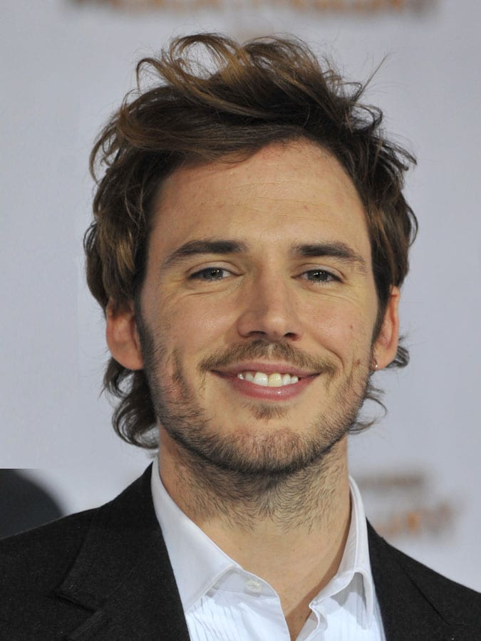 Smiling Sam Claflin in black coat with white shirt posing for camera and showing his Messy Curls - hairstyles of Hollywood actors