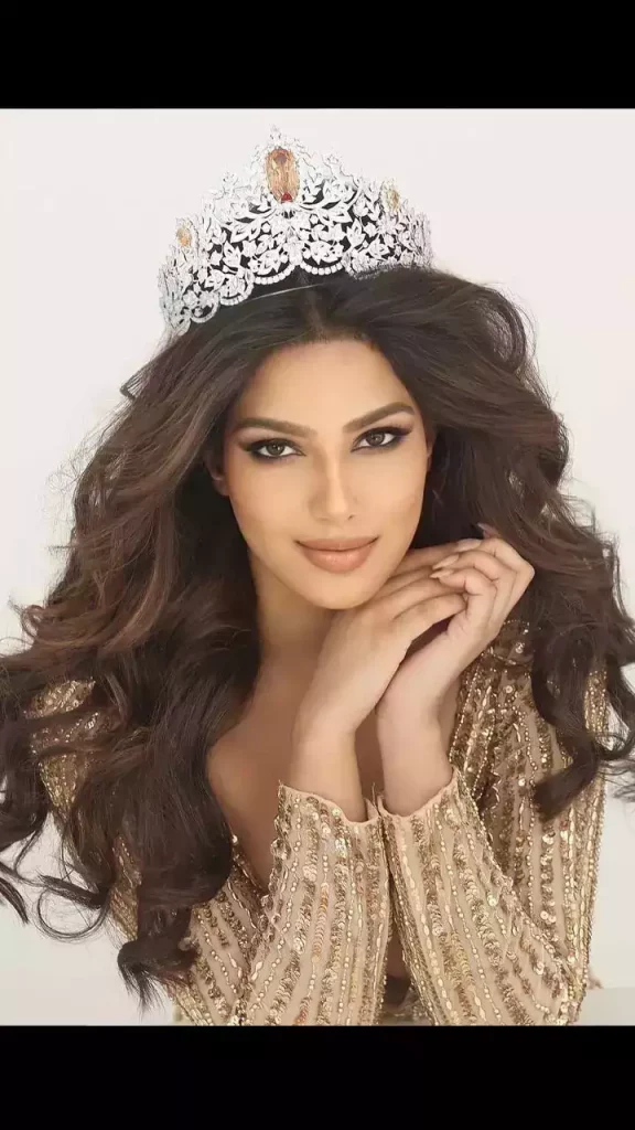 Harnaaz Sandhu in golden deep neck dress with Miss Universe crown posing for camera and showing her messy curls hairstyle - harnaaz sandhu images