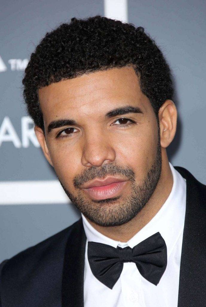 Drake in black coat with white shirt and black bow tie posing for camera and showing Short Afro hairstyle - hair style Hollywood