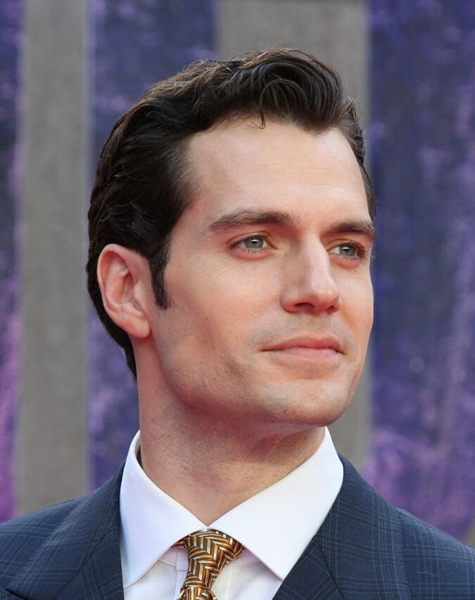 Smiling Henry Cavill in blue coat with white shirt and golden tie posing for camera and showing his Brush Up hairstyle - Hollywood heros hairstyle
