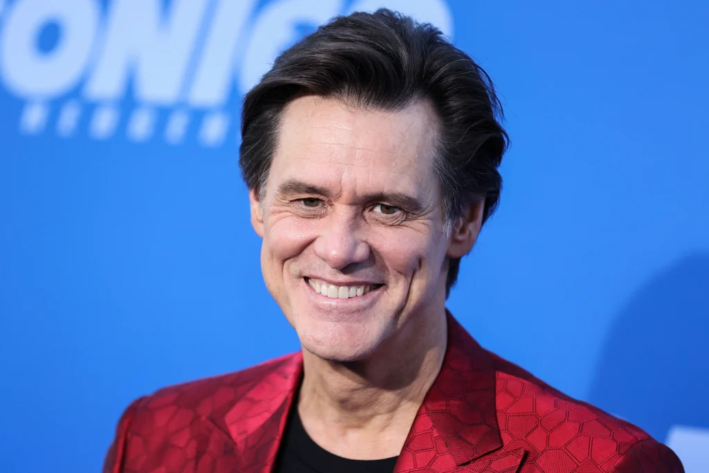 Smiling Jim Carrey in black t-shirt with self designed maroon coat posing for camera - dental implants hollywood celebrities