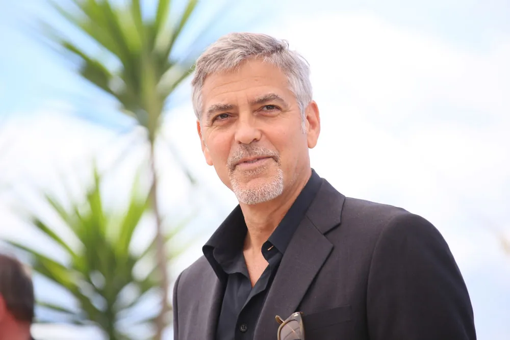 George Clooney in black shirt with grey coat posing for camera - Dental Implants