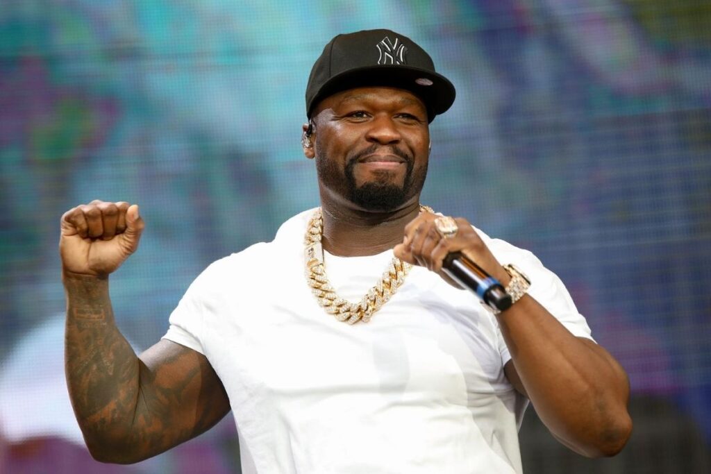 50 Cent in white t-shirt with thick golden chain and black cap holding mike in his hand - hollywood celebrities with dental implants