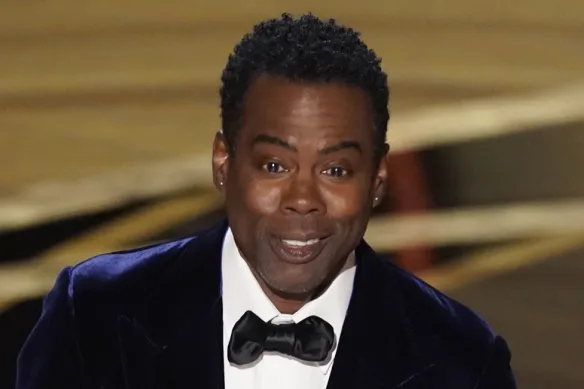 Smiling Chris Rock in white shirt with black coat and matching bow tie posing for camera - hollywood dental implants