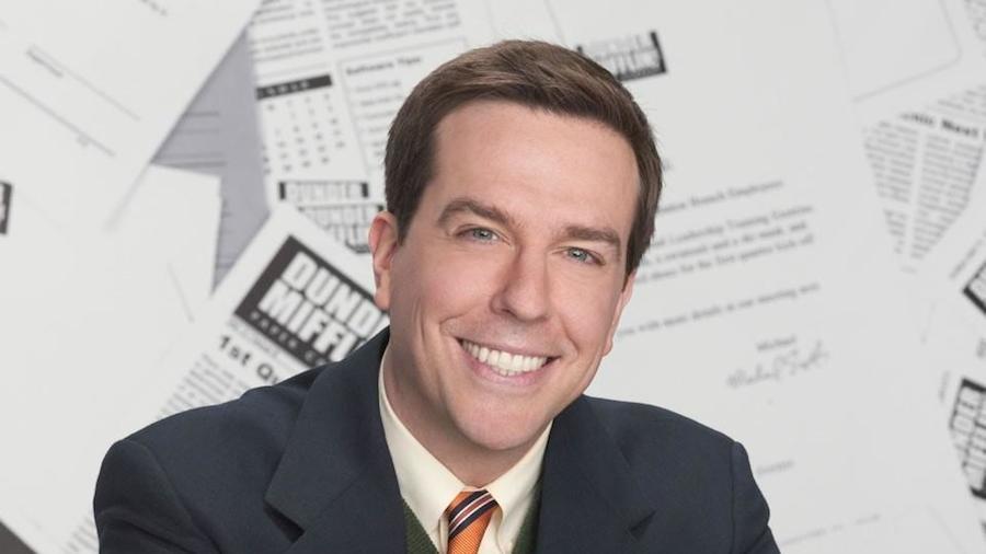 Smiling Ed Helms in white shirt with grey coat posing for camera - Dental Implants