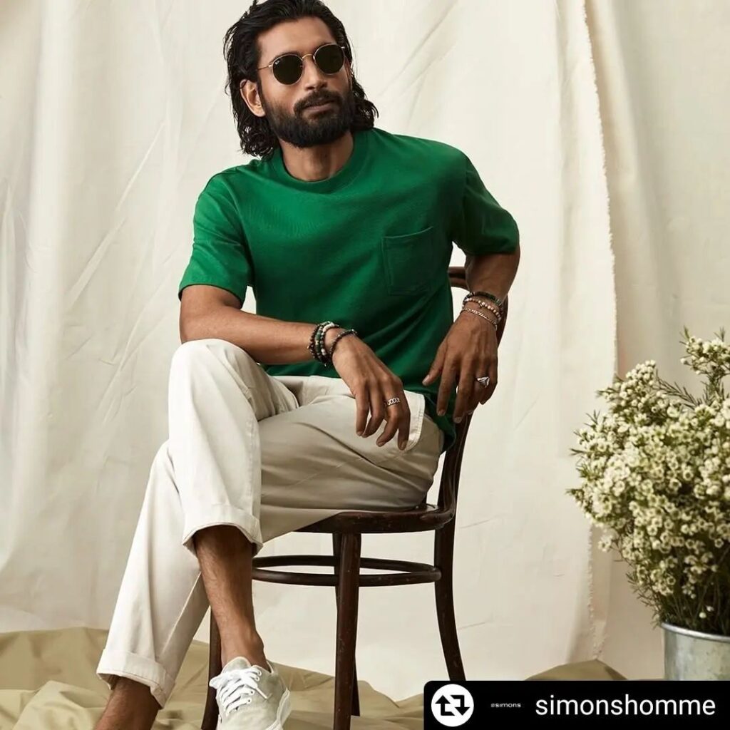 Himanshu Bhatti in green t-shirt with white pants and goggles sitting on a chair and posing for camera - male model images Indian