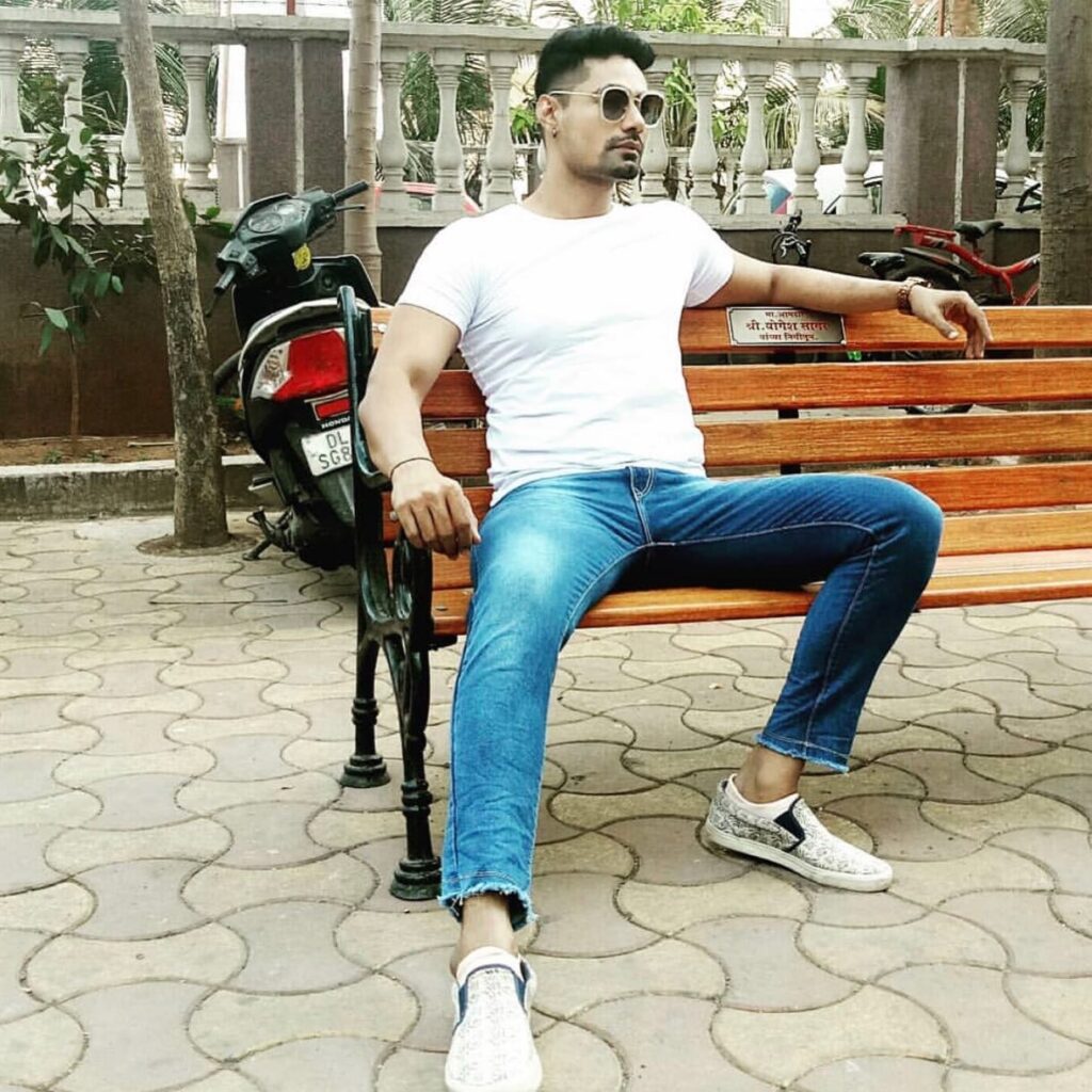 Meer Ali in white t-shirt , blue jeans and goggles sitting on a bench and posing for camera - male models of India
