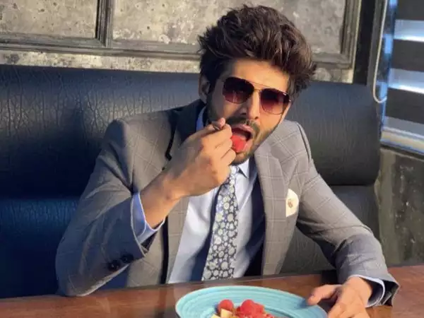 Kartik Aaryan in grey suit with matching tie and goggles eating some fruits with the help of a fork - Kartik Aaryan hair care routine