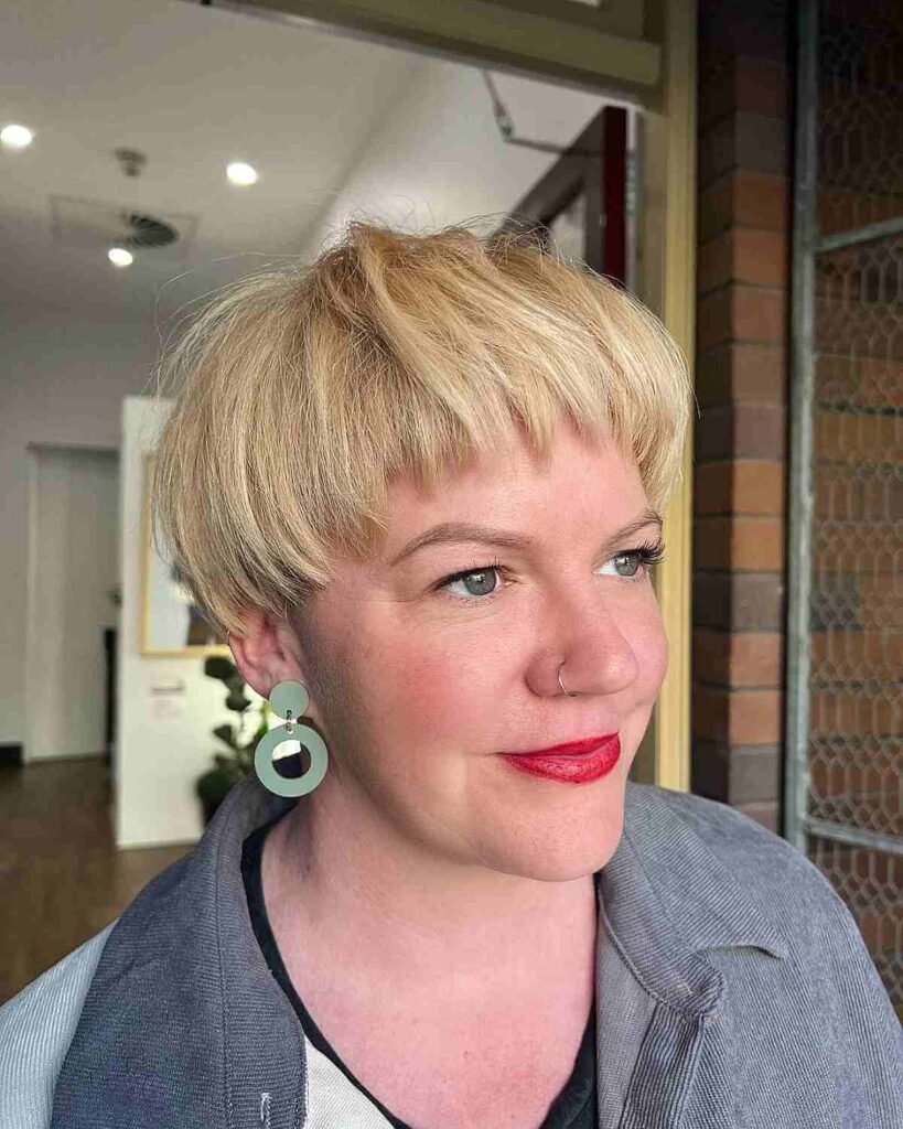 Woman in off white and grey jacket with red lipstick and earring posing for a selfie and showing her Trendy Bowl Cut hairstyle - short haircuts for women