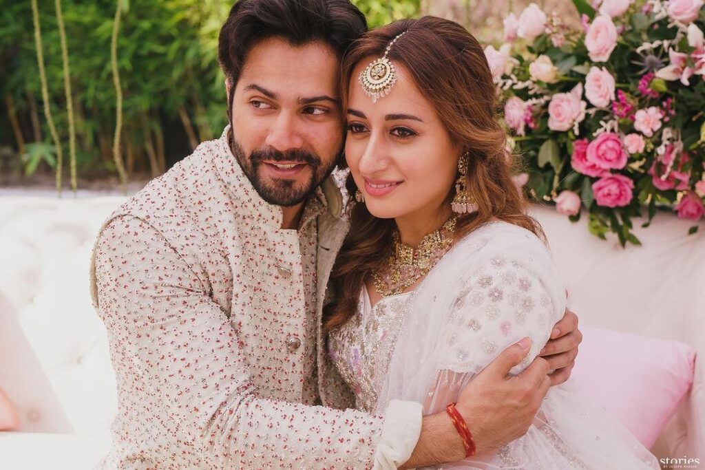 Varun Dhawan in pink and white kurta and Natasha in white lehenga with jewellery hugging each other and posing for camera - Taurus compatibility for love 