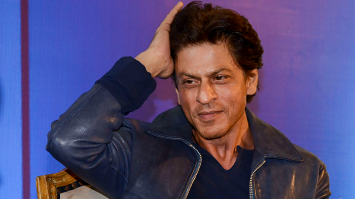 Shahrukh Khan in grey jacket and blue t-shirt posing for camera - Shahrukh Khan Hair Care Routine