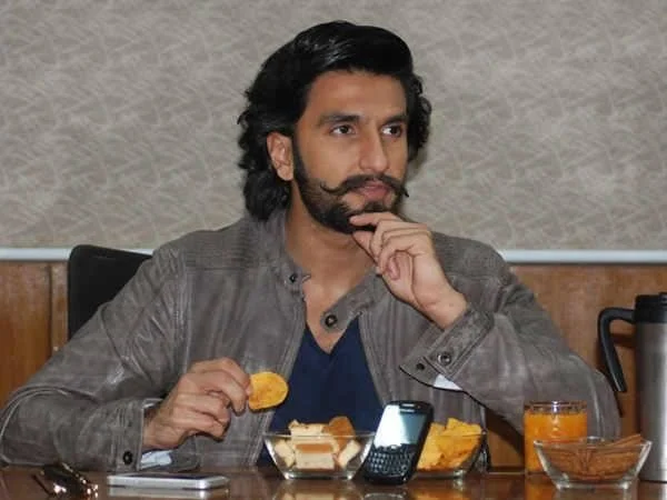 Ranveer Singh in grey jacket with blue t-shirt eating some snacks - Ranveer Singh hair look
